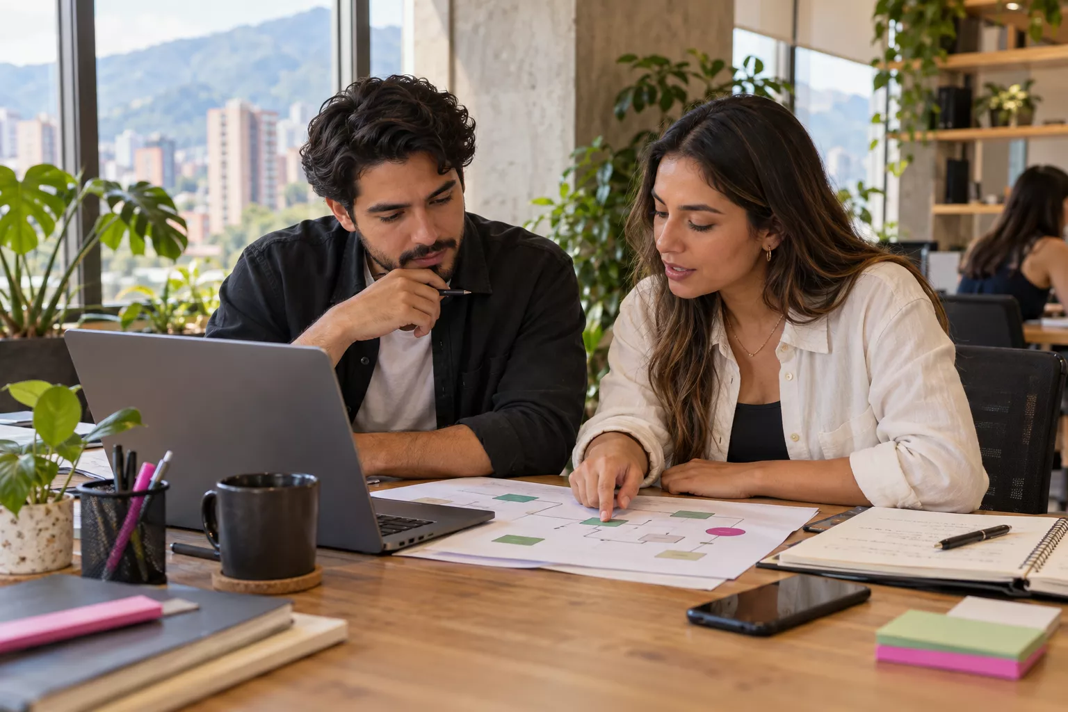 Dos profesionales revisando un diagrama de trabajo en papel junto a un portátil